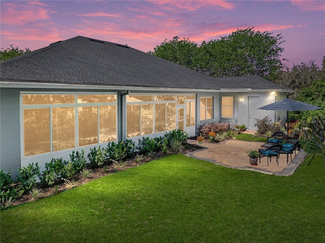 800 Osprey Landing Dr, Lakeland, FL 33813 - back of house at dusk with a patio area, roof with shingles, and a lawn