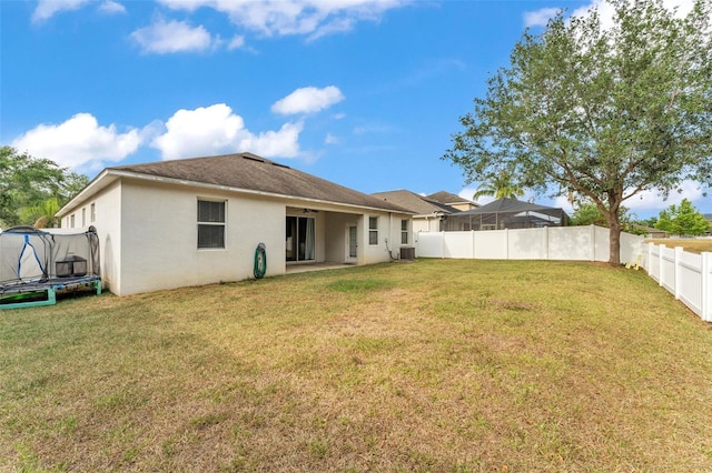 3592 Prescott Loop, Lakeland, FL 33810 - rear view of property with a trampoline, central AC unit, a fenced backyard, a yard, and stucco siding