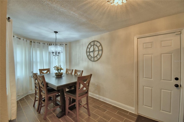 dining room with an inviting chandelier, baseboards, and a textured ceiling