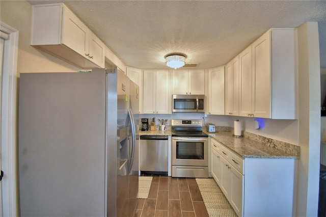 kitchen featuring wood tiled floor, a textured ceiling, light stone countertops, white cabinets, and stainless steel appliances