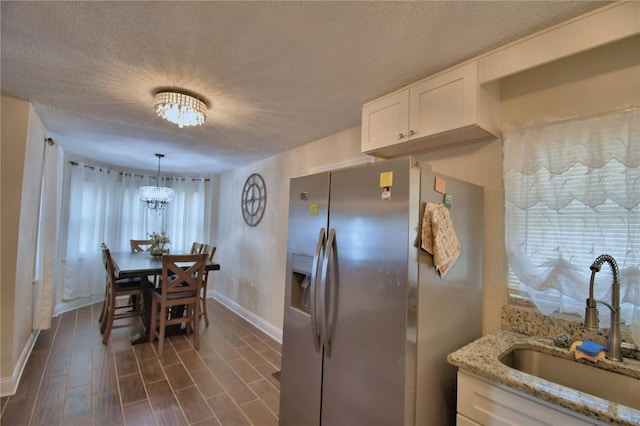 kitchen with a textured ceiling, a sink, stainless steel fridge with ice dispenser, white cabinets, and baseboards