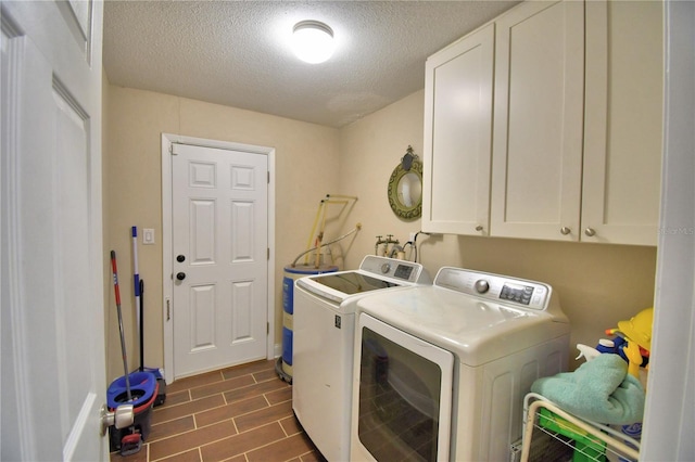 laundry area featuring water heater, cabinet space, a textured ceiling, and washing machine and clothes dryer