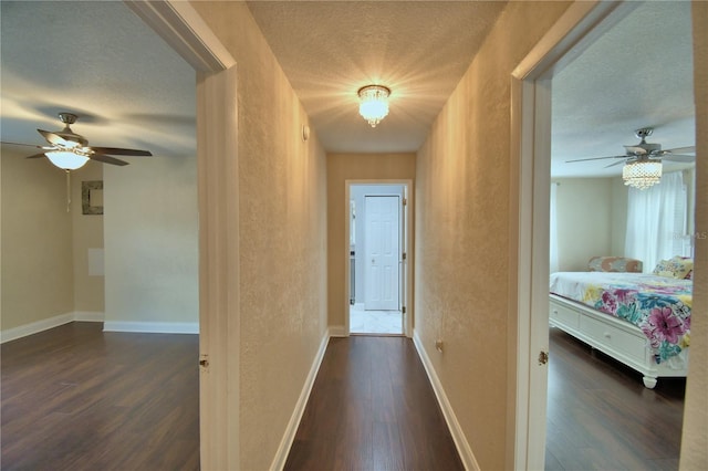 hallway with dark wood-style flooring, a textured ceiling, a textured wall, and baseboards