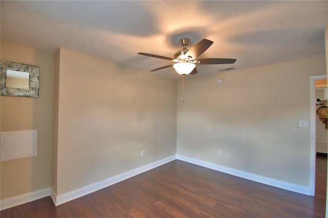 spare room featuring ceiling fan, visible vents, baseboards, and dark wood-type flooring
