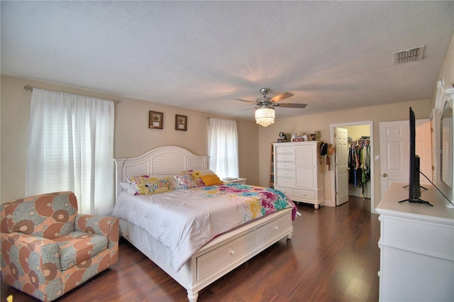 bedroom with visible vents, a closet, a walk in closet, a ceiling fan, and dark wood finished floors