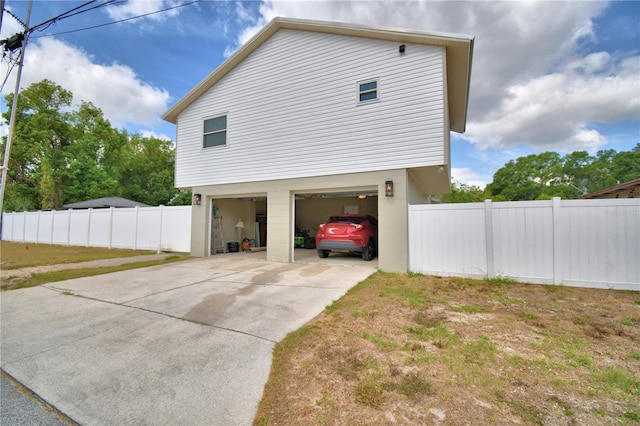 view of property exterior featuring fence, an attached garage, and driveway