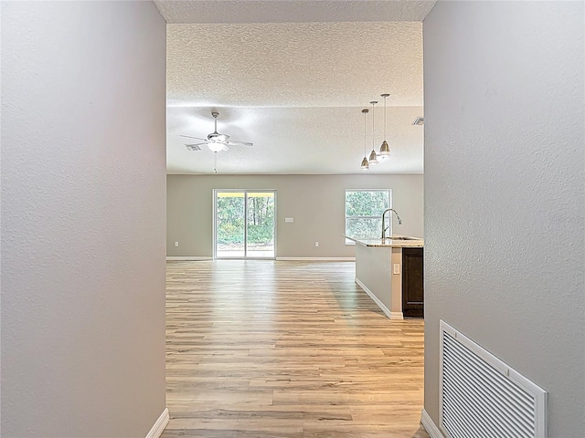 unfurnished room with light wood-type flooring, a textured ceiling, ceiling fan, a sink, and baseboards