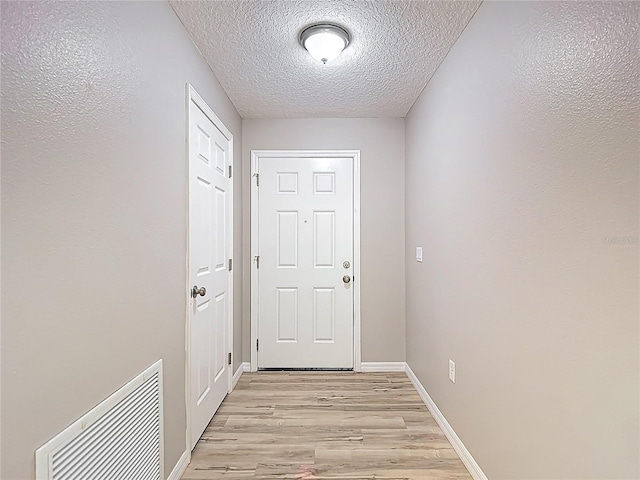 doorway to outside with light wood-style flooring, a textured ceiling, and baseboards