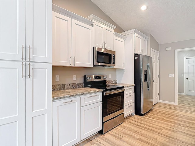 kitchen featuring stainless steel appliances, lofted ceiling, white cabinets, light wood-type flooring, and baseboards