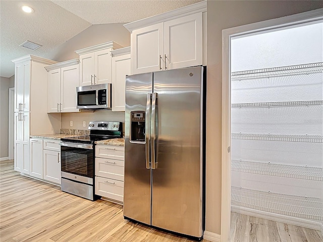 kitchen with stainless steel appliances, light wood-style flooring, lofted ceiling, white cabinets, and light stone countertops