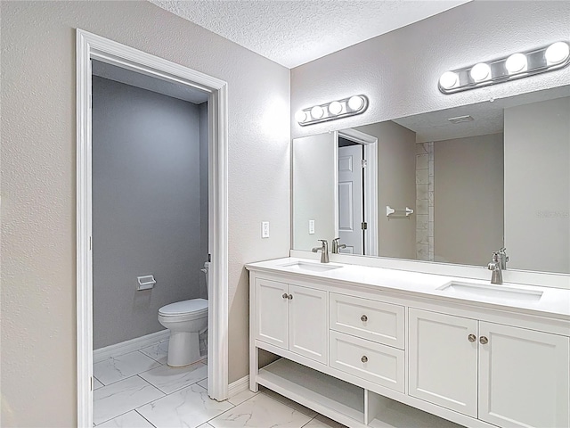 full bath with marble finish floors, toilet, double vanity, baseboards, and a textured wall