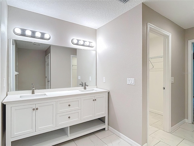 full bathroom with marble look tile flooring, baseboards, double vanity, a walk in closet, and a textured ceiling