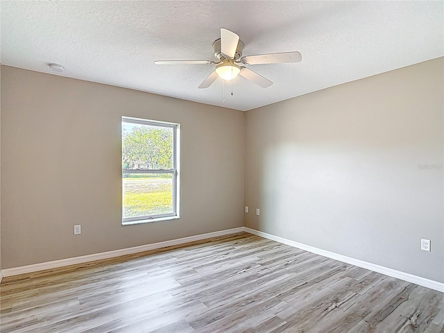 spare room featuring light wood-style flooring, a ceiling fan, baseboards, a smoke detector, and a textured ceiling