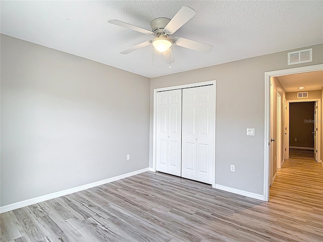unfurnished bedroom featuring light wood-type flooring, baseboards, a closet, ceiling fan, and a textured ceiling