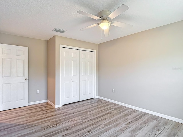unfurnished bedroom featuring light wood-style floors, a closet, baseboards, and a textured ceiling