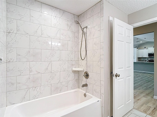 bathroom with a textured ceiling, tub / shower combination, a sink, and marble finish floors