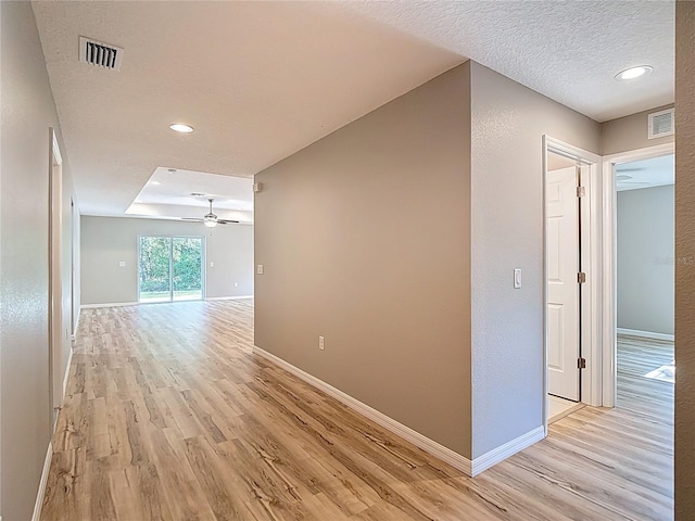 hall with light wood finished floors, baseboards, recessed lighting, and a textured ceiling