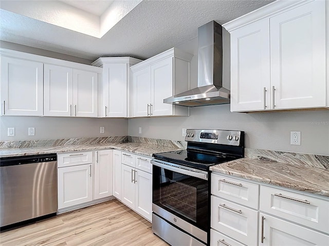 kitchen with appliances with stainless steel finishes, wall chimney range hood, white cabinetry, light wood-style floors, and a textured ceiling