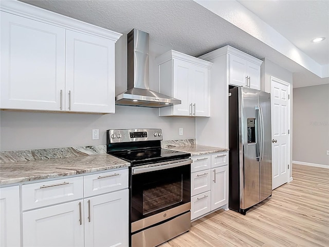 kitchen with stainless steel appliances, wall chimney range hood, light wood-type flooring, white cabinets, and baseboards
