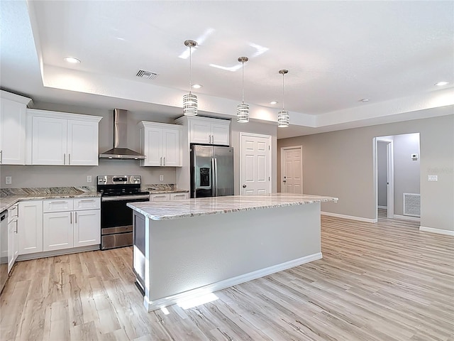 kitchen with appliances with stainless steel finishes, wall chimney range hood, light wood finished floors, a center island, and white cabinetry