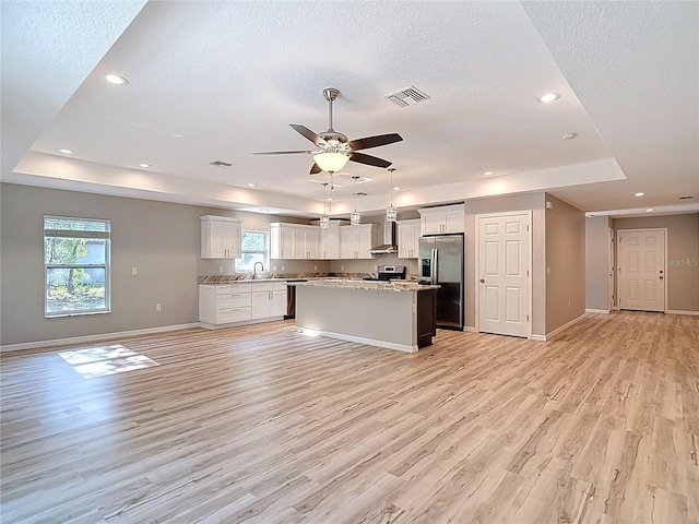 kitchen with stainless steel appliances, open floor plan, light wood finished floors, a raised ceiling, and recessed lighting