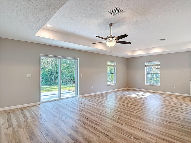 spare room featuring a raised ceiling, a textured ceiling, light wood finished floors, ceiling fan, and baseboards