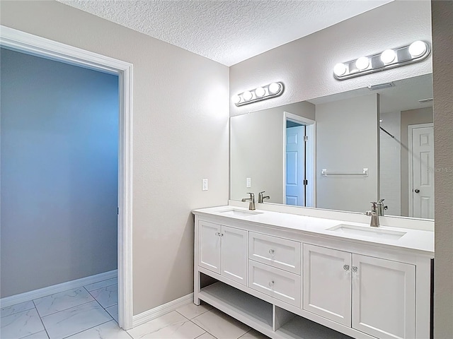 bathroom with marble look tile flooring, double vanity, baseboards, and a textured ceiling
