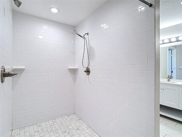 bathroom with a tile shower, vanity, and recessed lighting