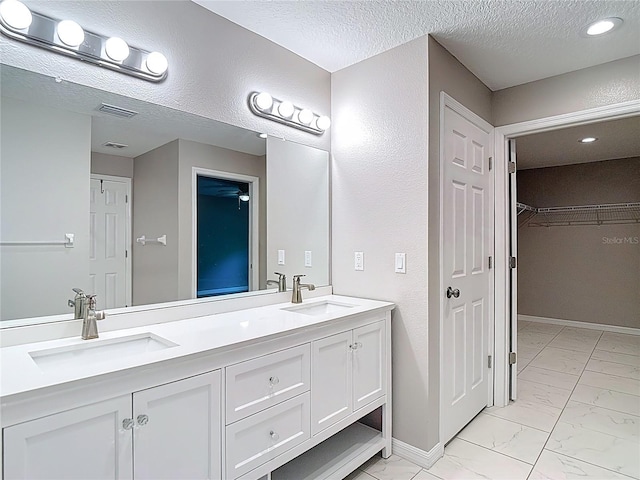bathroom featuring marble look tiles, double vanity, a textured ceiling, a walk in closet, and baseboards