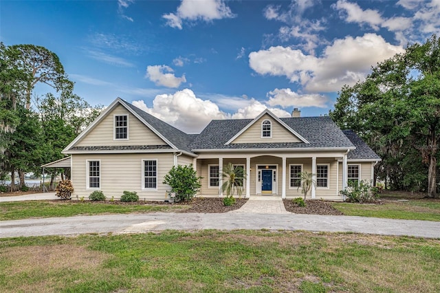 view of front of house with roof with shingles, covered porch, a chimney, and a front lawn
