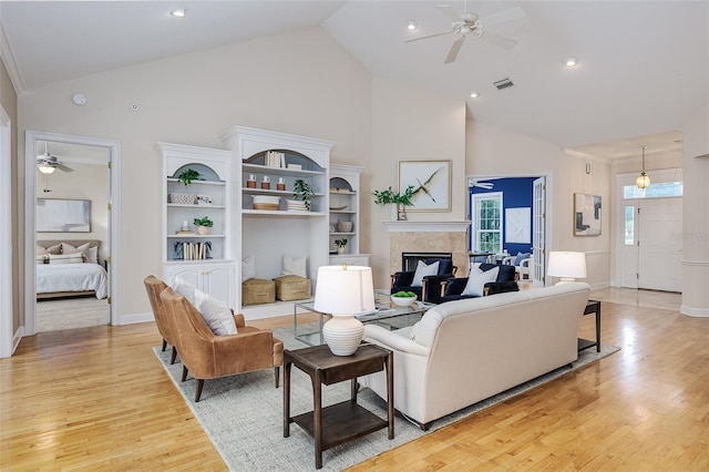 living area featuring light wood-type flooring, a ceiling fan, high vaulted ceiling, and a fireplace