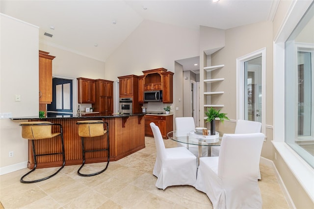 kitchen featuring a peninsula, dark countertops, a breakfast bar area, high vaulted ceiling, and appliances with stainless steel finishes