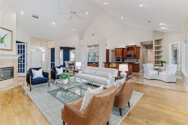 living room with visible vents, light wood-style floors, ceiling fan, high vaulted ceiling, and a premium fireplace