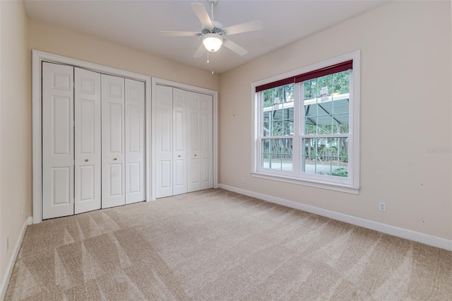 unfurnished bedroom featuring baseboards, a ceiling fan, two closets, and carpet