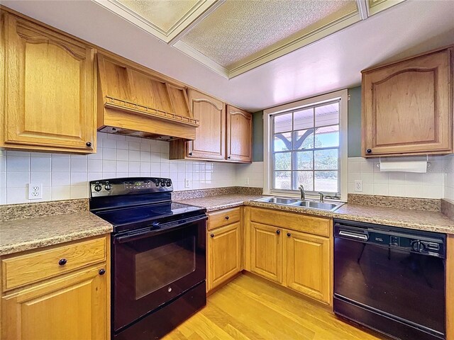 kitchen with a sink, light wood-style floors, premium range hood, decorative backsplash, and black appliances