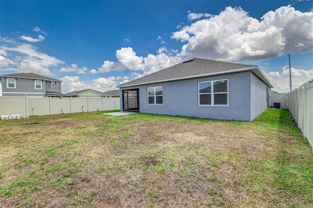 rear view of house featuring stucco siding, central AC unit, a fenced backyard, a yard, and roof with shingles