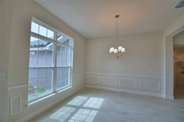 unfurnished dining area featuring a decorative wall, a chandelier, light wood-style flooring, a wainscoted wall, and visible vents