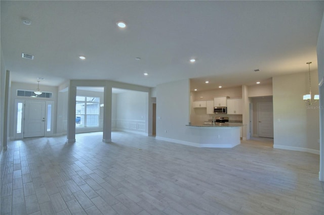 unfurnished living room with an inviting chandelier, light wood finished floors, recessed lighting, baseboards, and visible vents