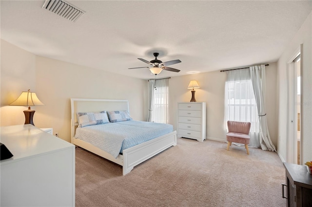bedroom featuring visible vents, a ceiling fan, light carpet, and multiple windows