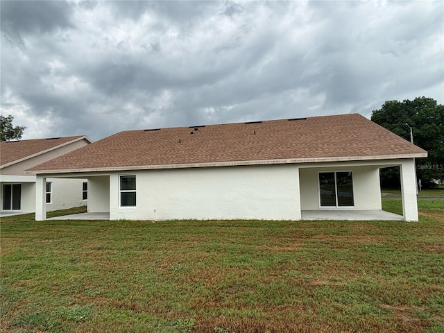 rear view of property with a patio, a lawn, stucco siding, and roof with shingles