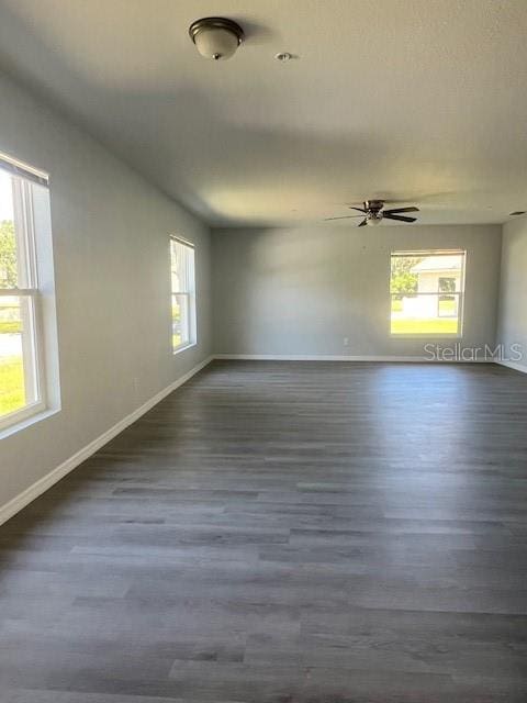 unfurnished room featuring baseboards, a ceiling fan, and dark wood-style flooring
