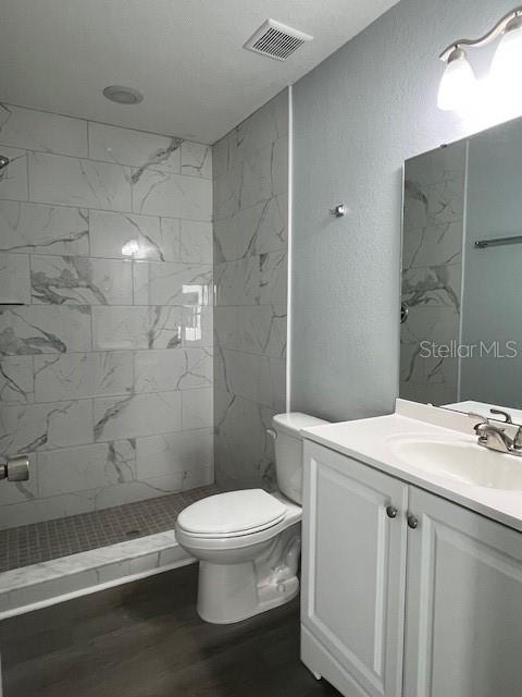 full bathroom with visible vents, walk in shower, vanity, toilet, and a textured wall