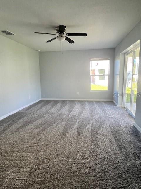 empty room with visible vents, carpet, baseboards, and a ceiling fan