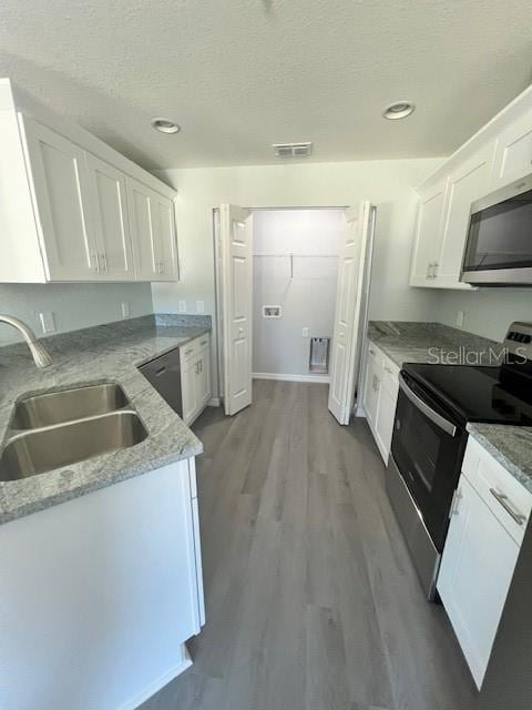 kitchen featuring white cabinets, light stone countertops, appliances with stainless steel finishes, a sink, and wood finished floors