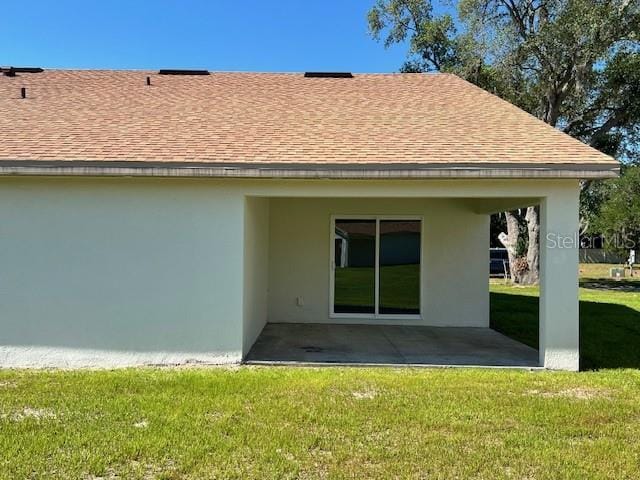back of house with stucco siding, roof with shingles, a patio area, and a yard