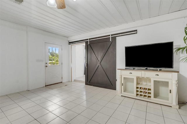 unfurnished living room with light tile patterned floors, visible vents, a barn door, and a ceiling fan