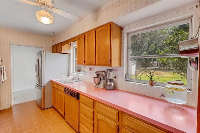 kitchen featuring freestanding refrigerator, wallpapered walls, dishwasher, a sink, and light countertops