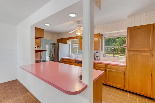 kitchen featuring a peninsula, stainless steel fridge, wallpapered walls, ceiling fan, and light countertops