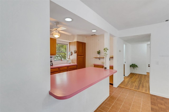 kitchen featuring wallpapered walls, baseboards, a ceiling fan, and brown cabinets
