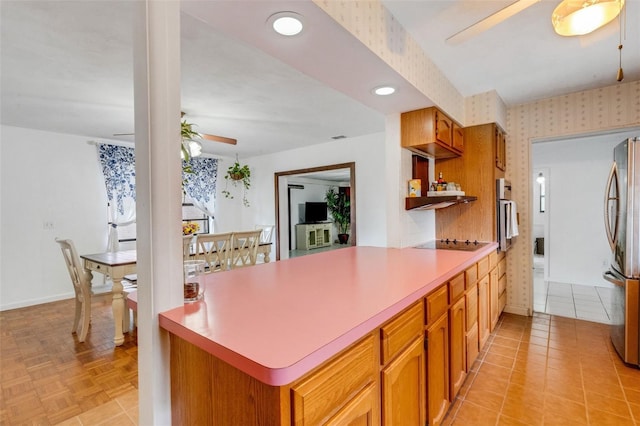 kitchen with a peninsula, a ceiling fan, wallpapered walls, extractor fan, and appliances with stainless steel finishes